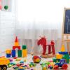 A room with colorful toys strewn about the ground. There is a window with the curtains drawn.