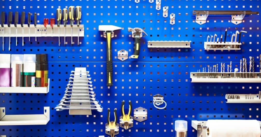 A variety of tools are hanging on a blue board. Some of the tools are hammers, wrenches, and screwdrivers.