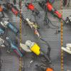 Many power tools are hanging from a wall rack. Among the tools are power saws and some drills.