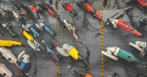 Many power tools are hanging from a wall rack. Among the tools are power saws and some drills.