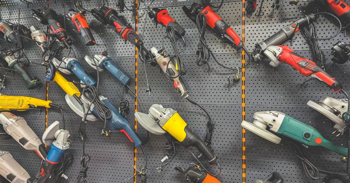 Many power tools are hanging from a wall rack. Among the tools are power saws and some drills.