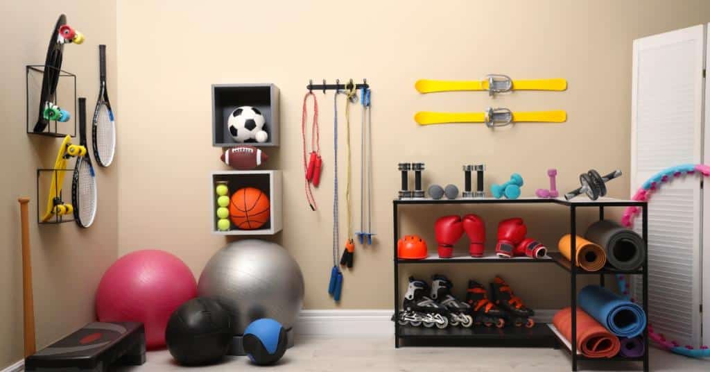 A room is filled with all sorts of items, such as exercise balls, boxing gloves, weights, and skis that are hanging on the wall.
