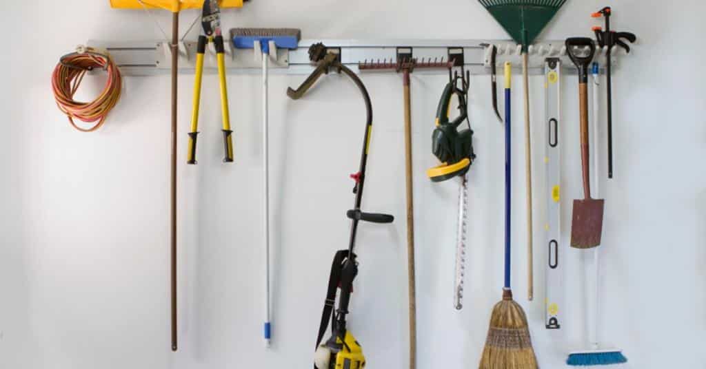 Several pieces of gardening equipment are hanging on the wall. There is a rake, hedge clippers, and a shovel.