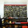 Tools are hanging on some wall storage. There is also a ladder to the side of the tool wall hangings.