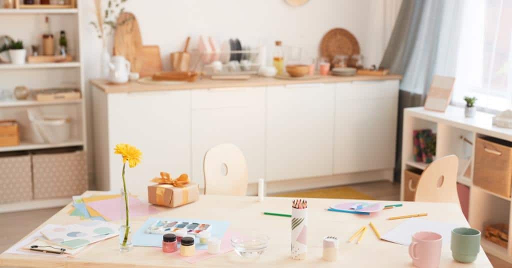 A craft room with a desk that has several pieces of art materials on it, such as paint, paper, and brushes.