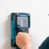 A person is using a device and pressing it against a wall. They are also holding a pencil in their other hand.