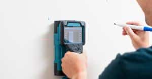 A person is using a device and pressing it against a wall. They are also holding a pencil in their other hand.