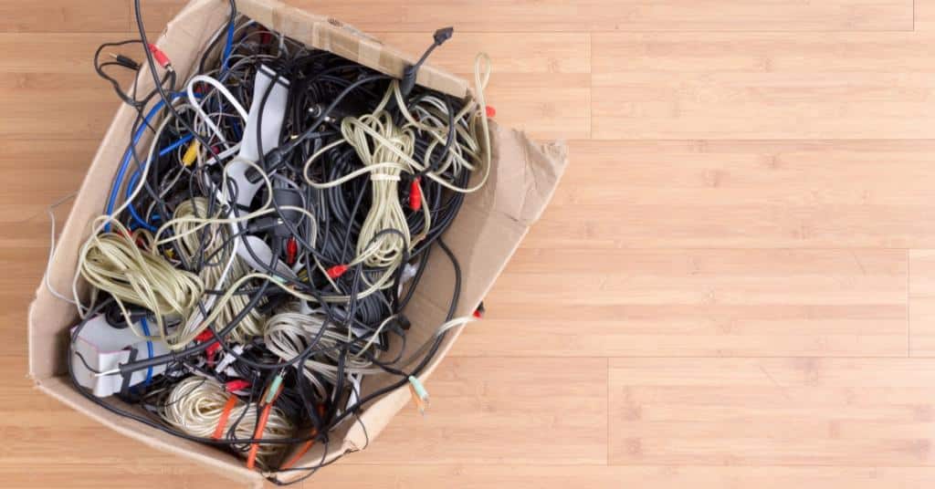 A cardboard box is filled with many different cords. A lot of the cords look old and frayed.