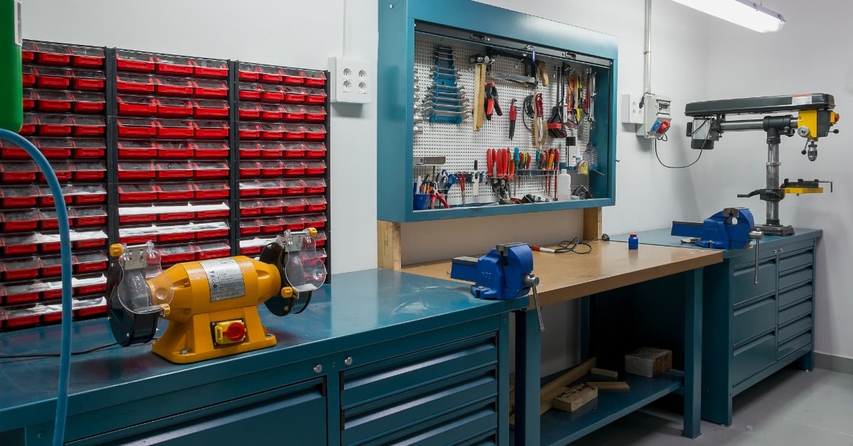 A workshop with tools and tables pushed up against the wall. The walls are white and without decoration.