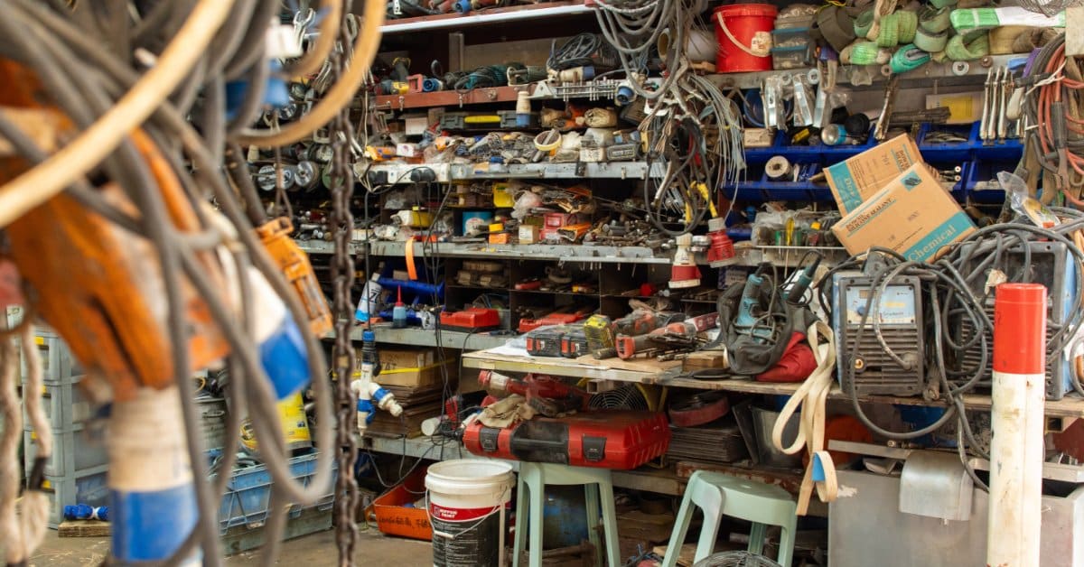 A workshop with hundreds of tools and other materials. There is a workbench that is also covered in clutter.