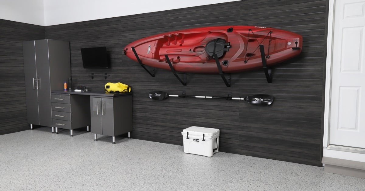 A red kayak is hanging from a slatwall system. The slatwalls are black and they are installed on a white wall.