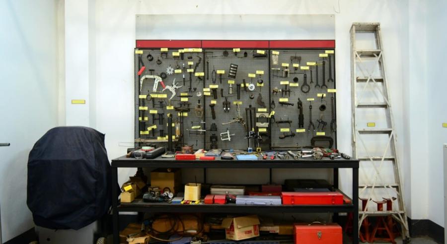 Tools are hanging on some wall storage. There is also a ladder to the side of the tool wall hangings.
