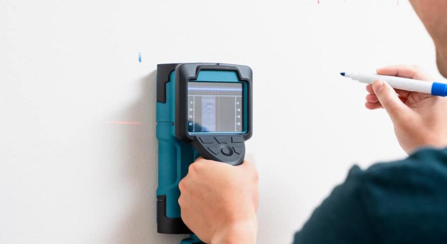 A person is using a device and pressing it against a wall. They are also holding a pencil in their other hand.
